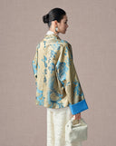 Back view of a women’s gold jacquard jacket featuring blue floral and phoenix motifs