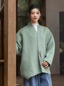 Model wearing the sage green Ningyuan coat, showing its V neckline and button with a dangling beaded cord.