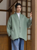 Model wearing the Ningyuan sage green coat with one hand in a pocket and the other resting on a wooden pillar.