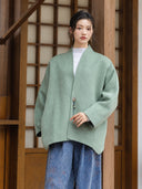 Model wearing the Ningyuan sage green coat over a white knit top with patterned blue trousers.
