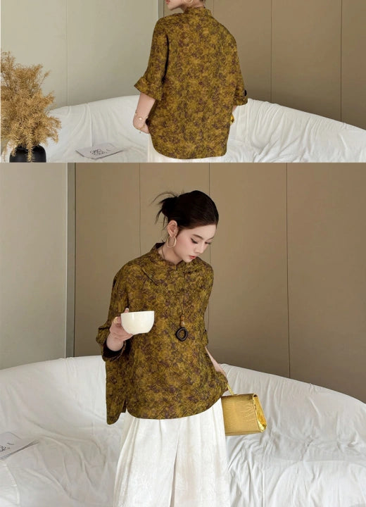 Woman wearing an olive floral cheongsam-style top with a white skirt, styled in a vintage elegant setting with a teacup and small handbag.
