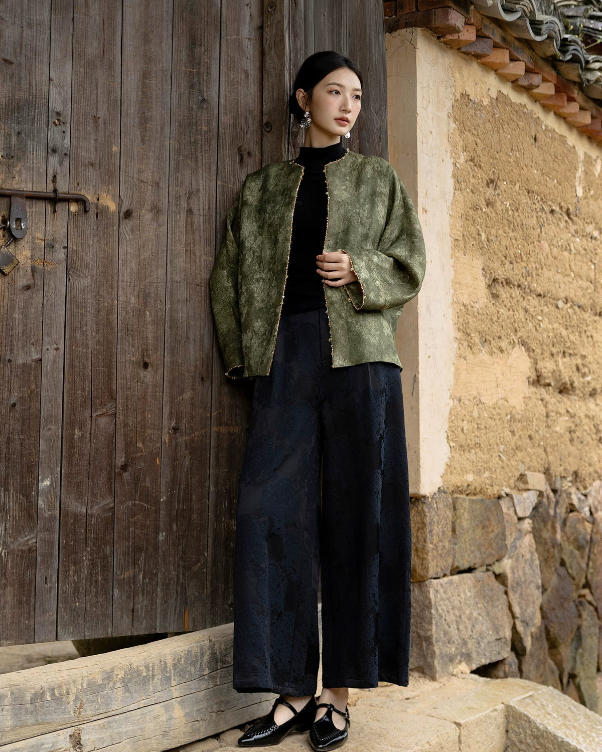 Full-length outfit featuring an olive floral jacket, a black top, dark wide-leg patterned trousers and black shoes.