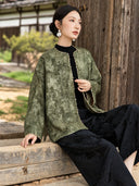 Seated view of an olive jacket showing its tonal floral pattern, softly mottled colour and gold-tone edging along the front and cuffs.