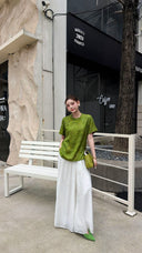 Front view of a women's green Qipao top with mandarin collar and asymmetric button detail, styled with white flowy trousers.