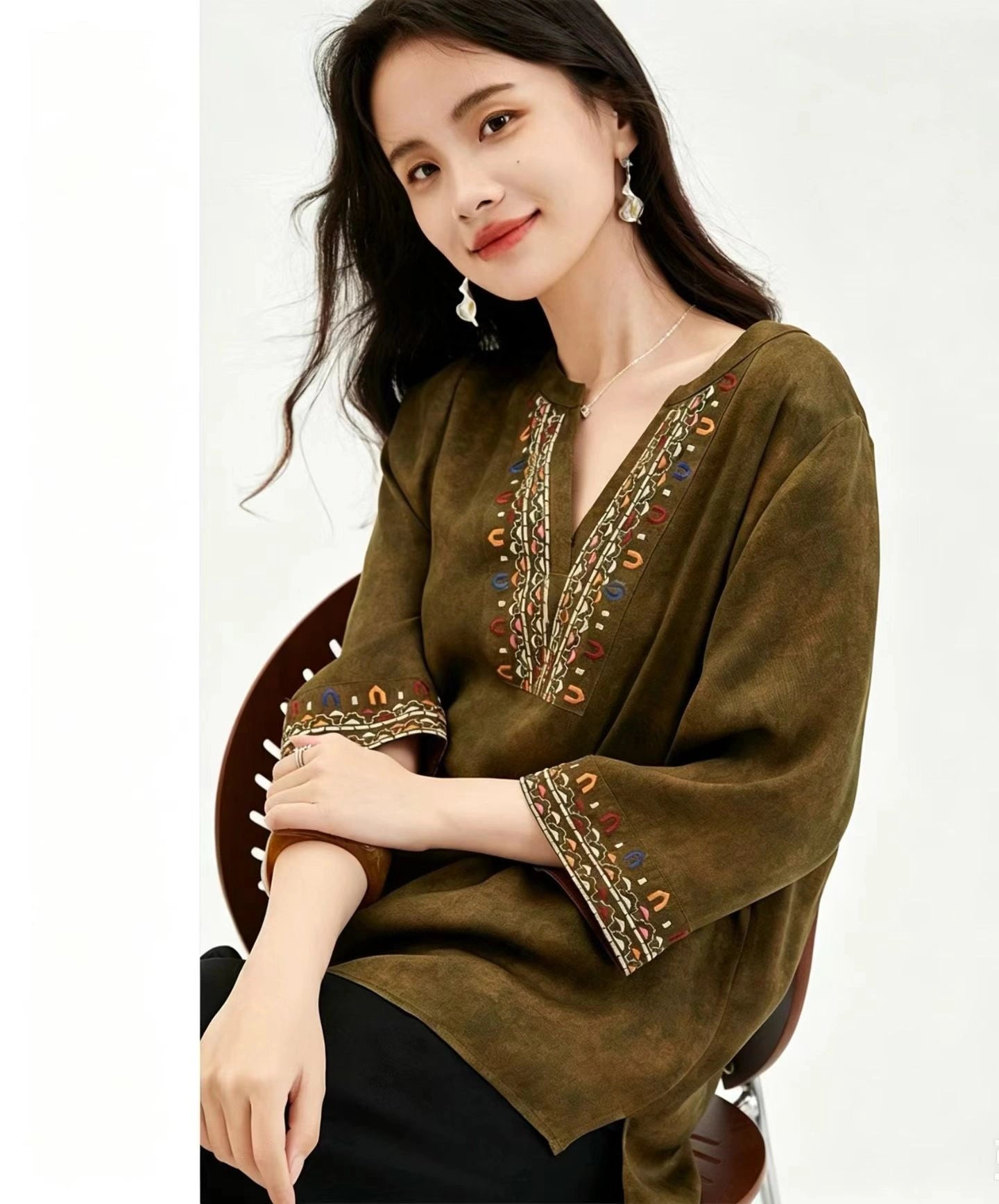 Close-up of a dark olive green silk top with a V-neckline and intricate multicolor embroidery along the neckline and cuffs, emphasizing the texture and handcrafted details.