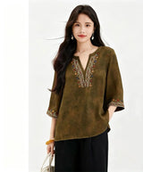 Front view of a loose-fit olive green silk tunic top with a V-neck and embroidered sleeves, paired with black wide-leg pants, crafted from 100% mulberry silk.