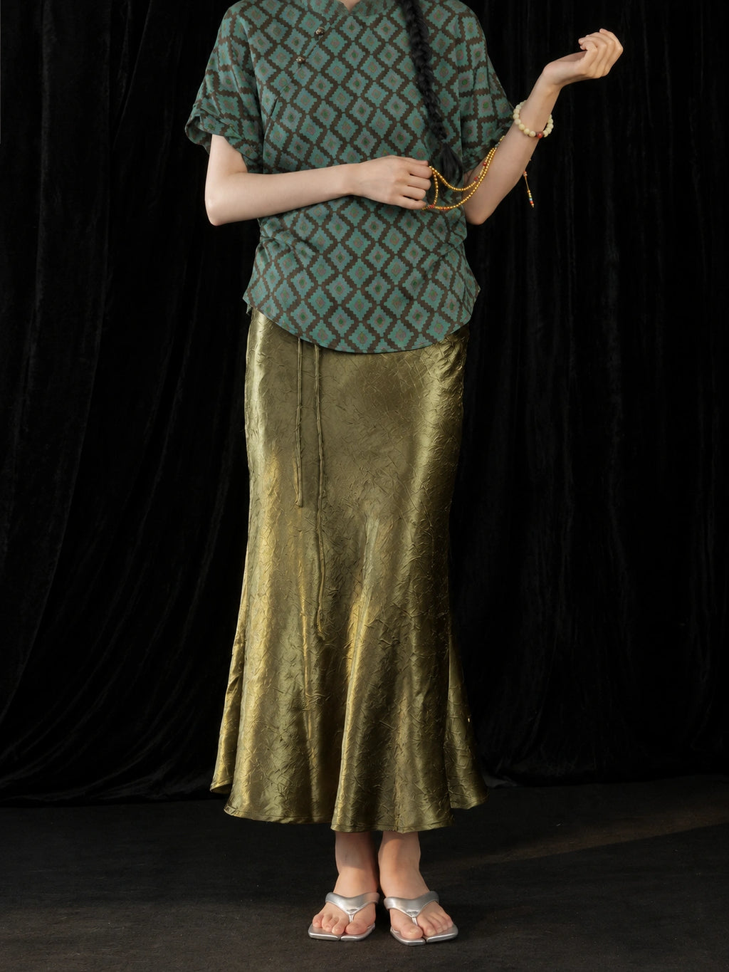 Detail view of the olive green high-sheen fishtail skirt showing its subtle crinkled texture and flowing hem