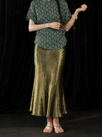 Detail view of the olive green high-sheen fishtail skirt showing its subtle crinkled texture and flowing hem