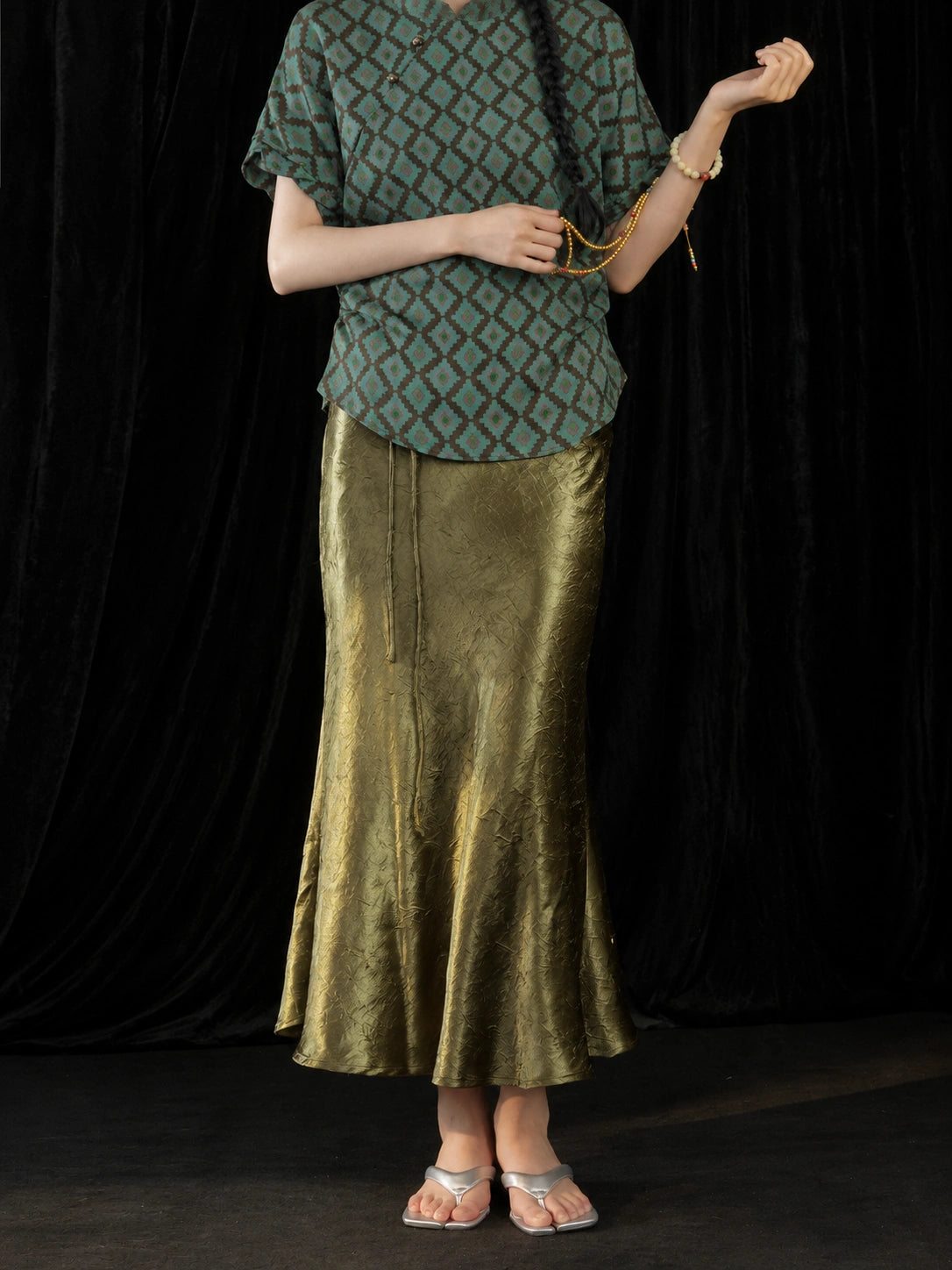Detail view of the olive green high-sheen fishtail skirt showing its subtle crinkled texture and flowing hem