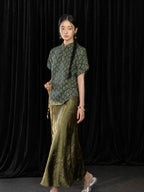 Model wearing an olive green high-sheen pleated fishtail skirt with a Chinese-style patterned top