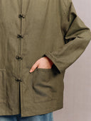 Close-up of the olive green jacket’s fabric, frog-button closure and front patch pocket