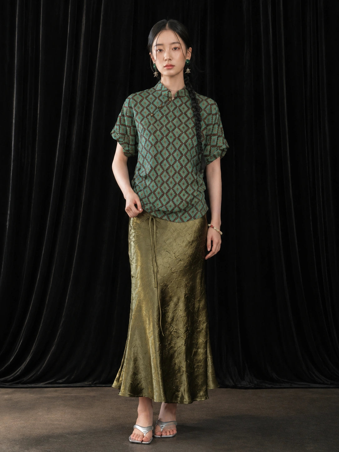 Front view of the olive green pleated fishtail skirt with a soft glossy finish and A-line silhouette