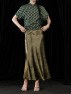 Close-up of the olive green pleated fishtail skirt waist and glossy textured fabric