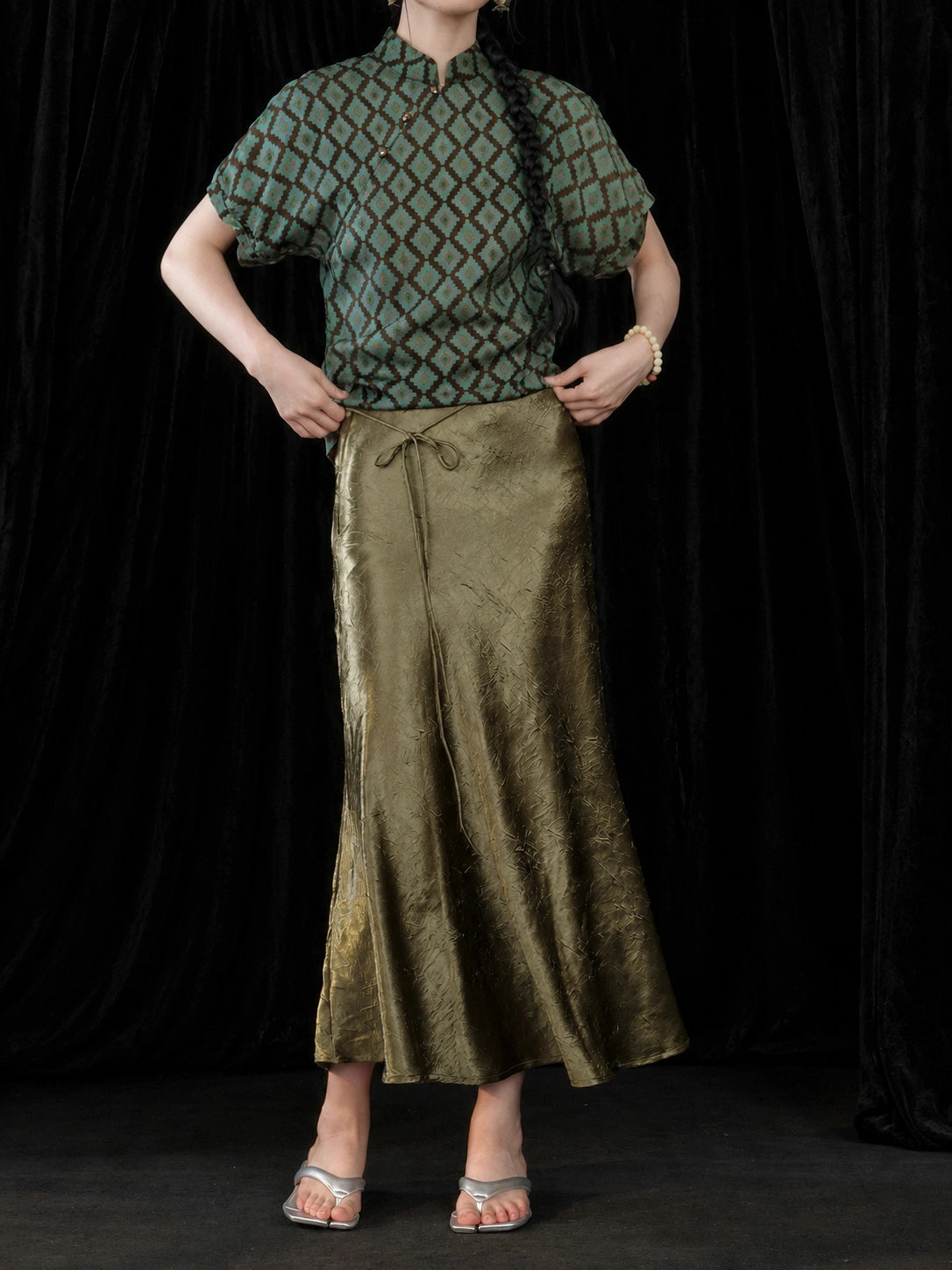 Close-up of the olive green pleated fishtail skirt waist and glossy textured fabric