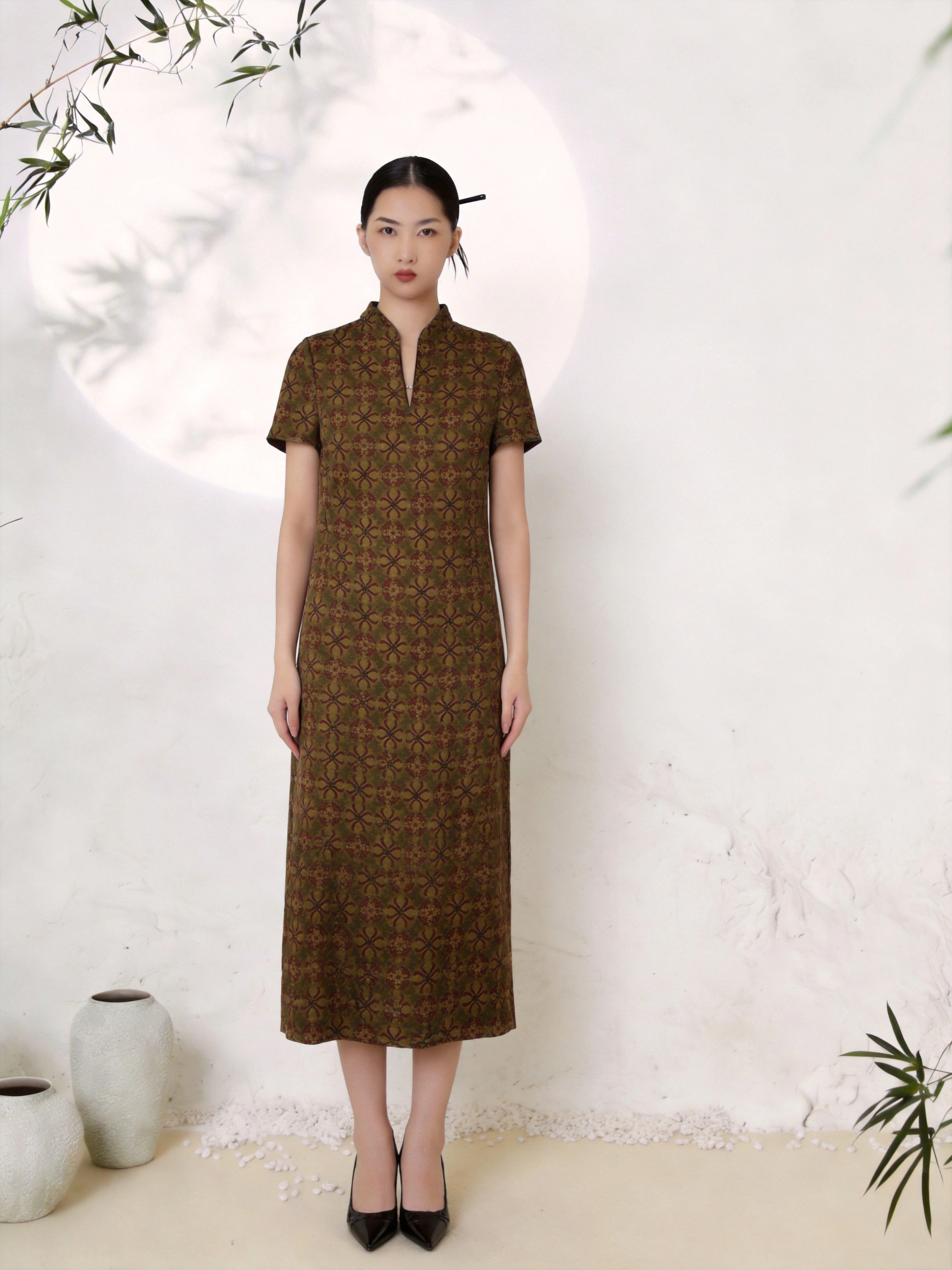 Full body shot of an olive green silk Cheongsam dress with a mandarin collar, V-slit neckline, short sleeves, and a geometric jacquard pattern, crafted from 100% mulberry silk, midi length with a straight A-line silhouette.