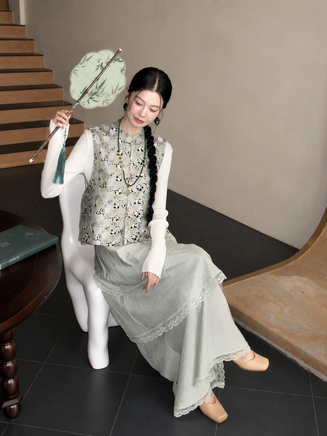 Seated model wearing a pale green Chinese-style silk vest with playful bear motifs and traditional detailing.