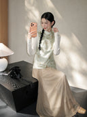 Seated model wearing a pale mint Chinese-style silk vest with delicate cat and butterfly motifs.