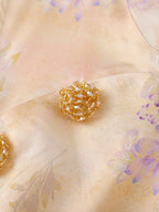 Close-up of the sparkling floral button and asymmetrical neckline on the peach viscose top.