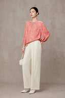 Angled full-length view of the peach pink blouse and cream trousers