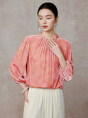 Close view of the blouse’s pleated neckline and pearl-like accents