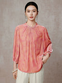 Model wearing a peach pink blouse with a pleated neckline and three-quarter sleeves