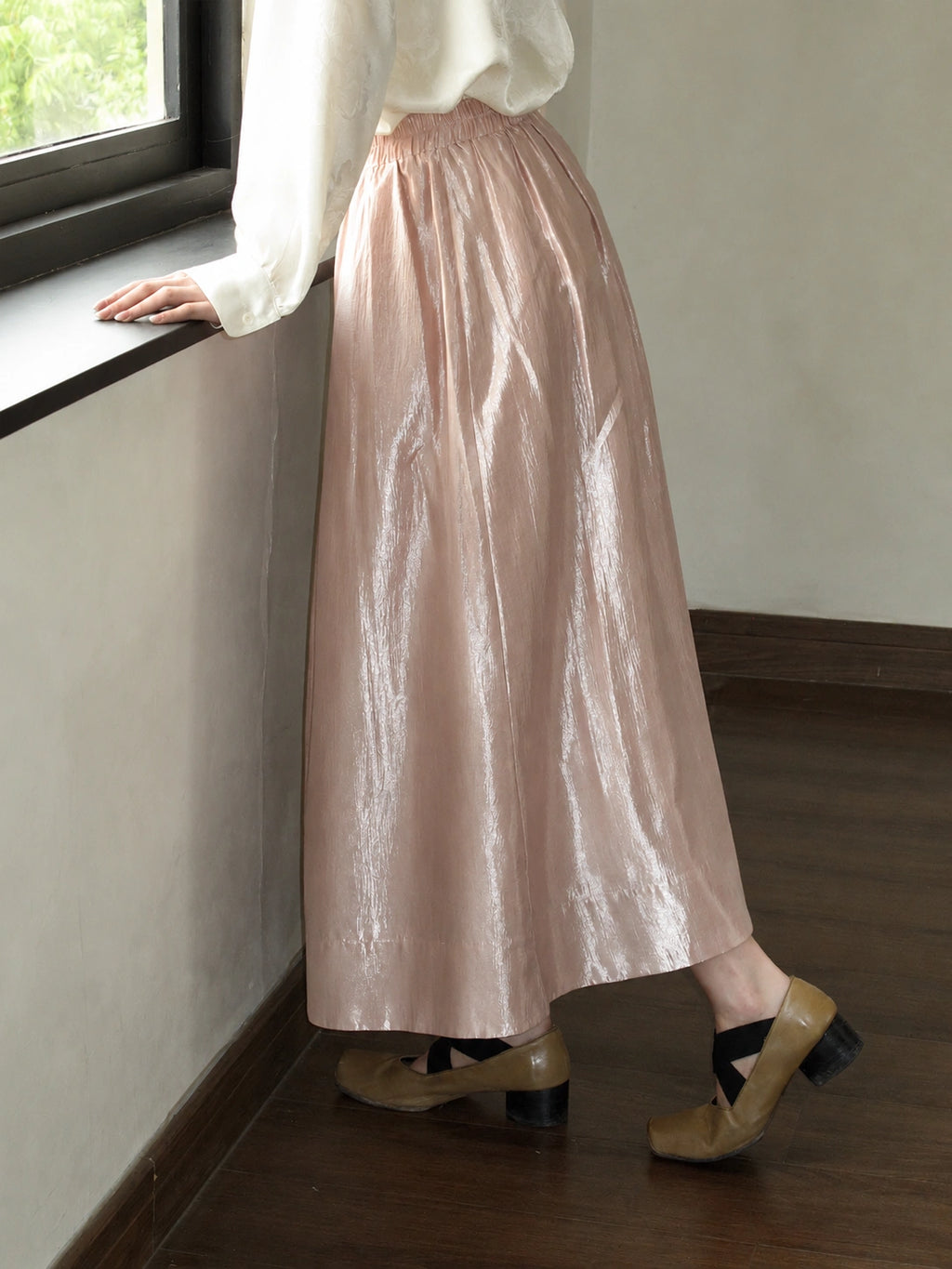 Side detail of a pink acetate-blend A-line skirt with a high waist, gathered waistband, and smooth ankle-length drape.