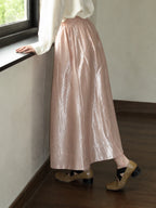 Side detail of a pink acetate-blend A-line skirt with a high waist, gathered waistband, and smooth ankle-length drape.