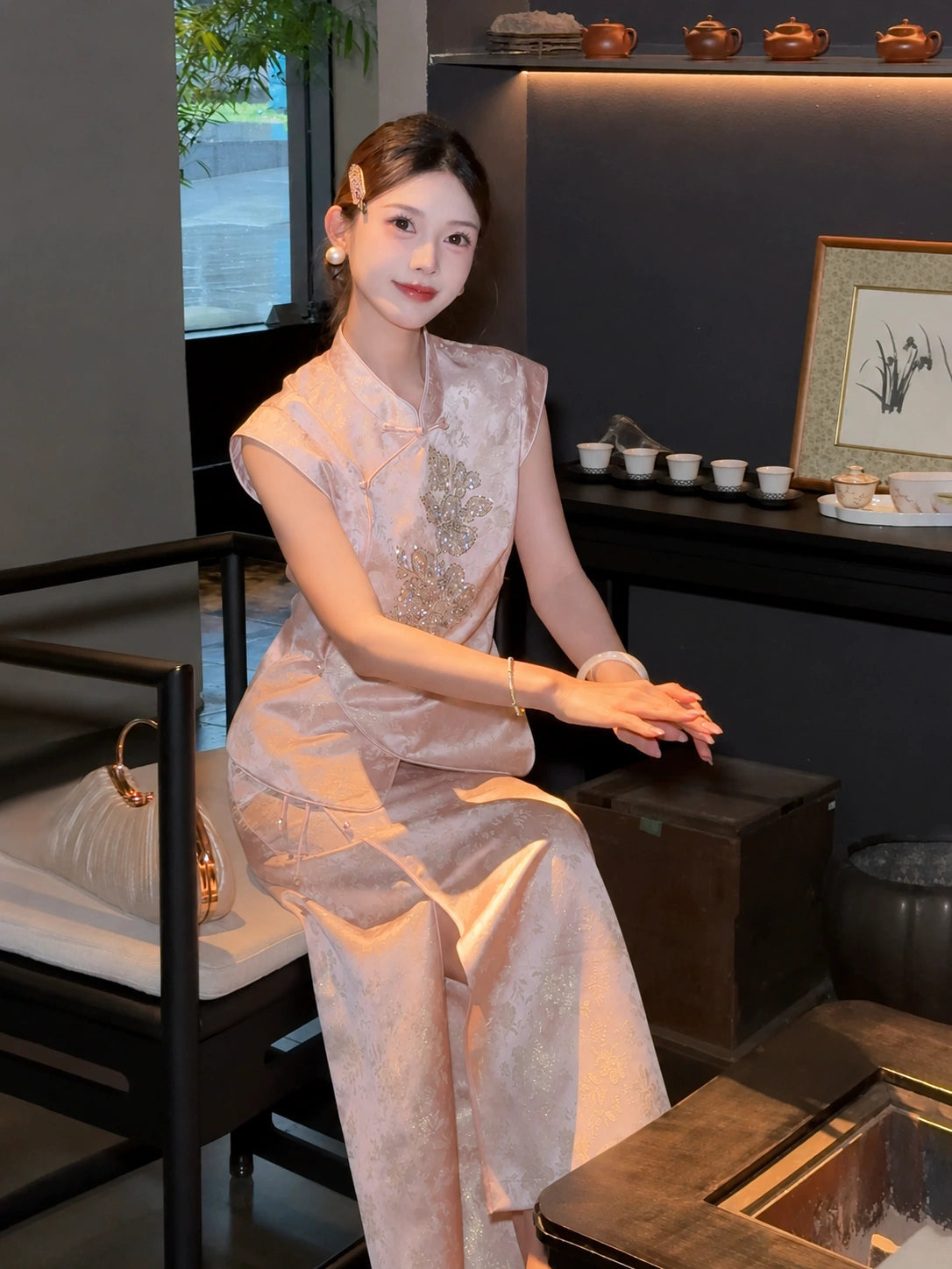 Sitting model in a pink Cheongsam top with sequin floral embroidery and matching skirt, showcasing the elegant fit and drape of the fabric.