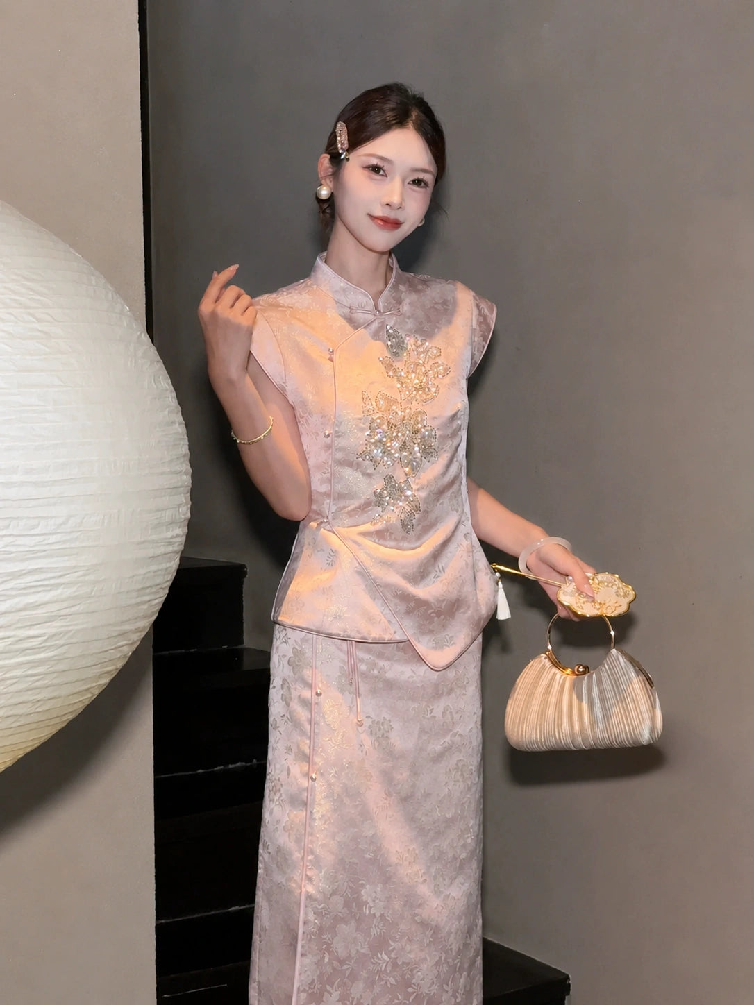 Side view of a pink cap-sleeve Cheongsam top with silver bead embroidery, styled with a matching skirt and a gold handbag.
