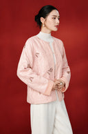 Angled front view of the pink jacket, showing the round neckline, textured surface and butterfly embellishments.
