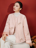 Seated model wearing the pink butterfly embroidered jacket with a white top and trousers.