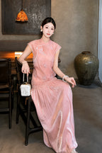 Sitting model in a pink Cheongsam dress with a mandarin collar, delicate embroidery, and a pleated skirt, holding a small bag, showcasing the relaxed fit.