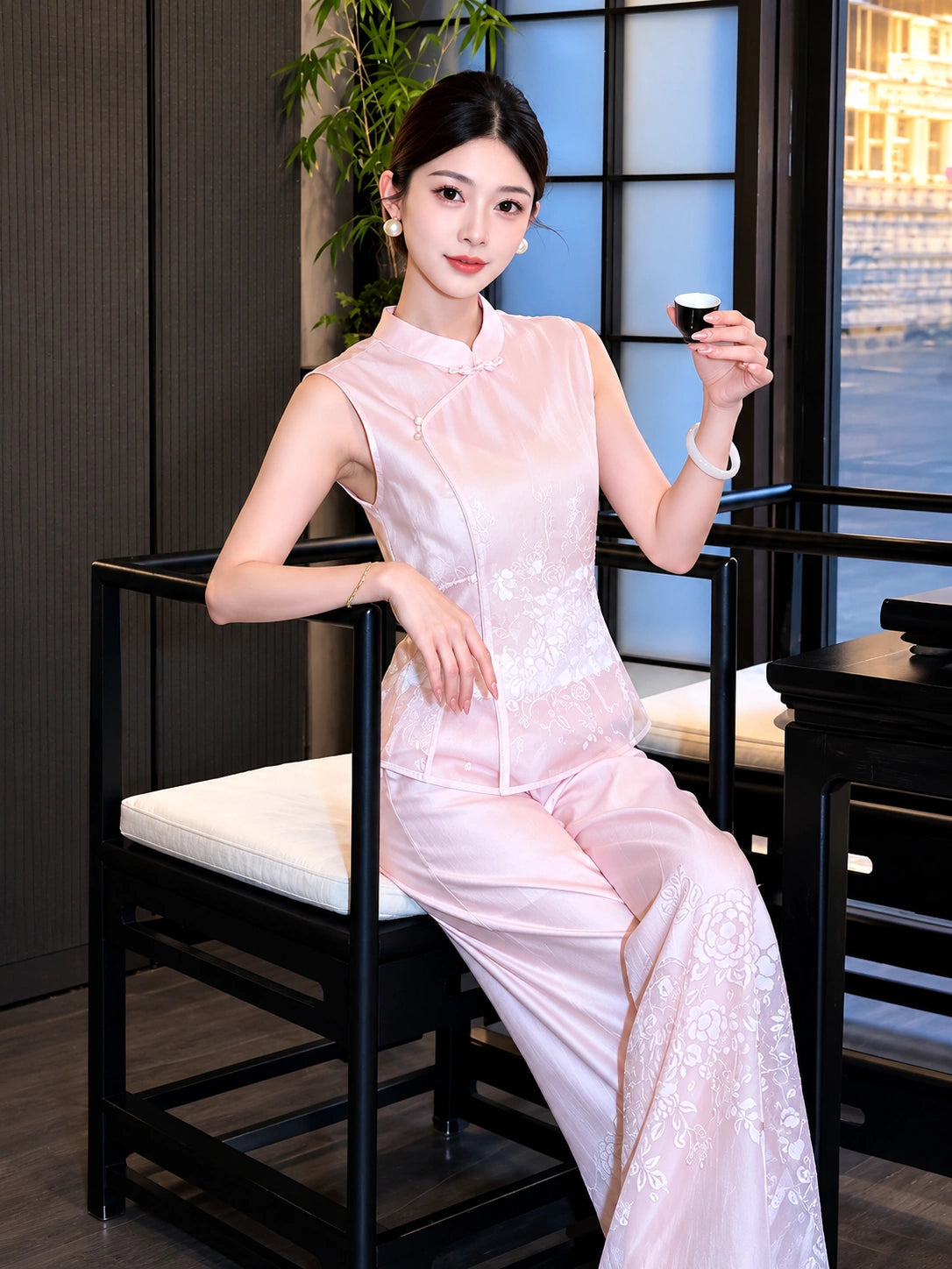Model sitting in a pink Cheongsam blouse and trousers co-ord set, holding a small tea cup, showcasing the elegant fit.