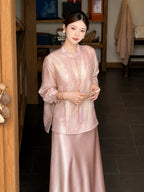 Model wearing a pink long-sleeve embroidered Cheongsam blouse with a matching satin skirt, holding a fan, showcasing the elegant 100% polyamide fabric.
