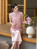 Sitting model wearing a pink sleeveless embroidered Cheongsam vest with a matching satin skirt, holding a folding fan, crafted from 100% polyester.
