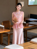 Full body shot of a pink embroidered Cheongsam vest and satin skirt set, styled with a folding fan and pearl earrings, 100% polyester.