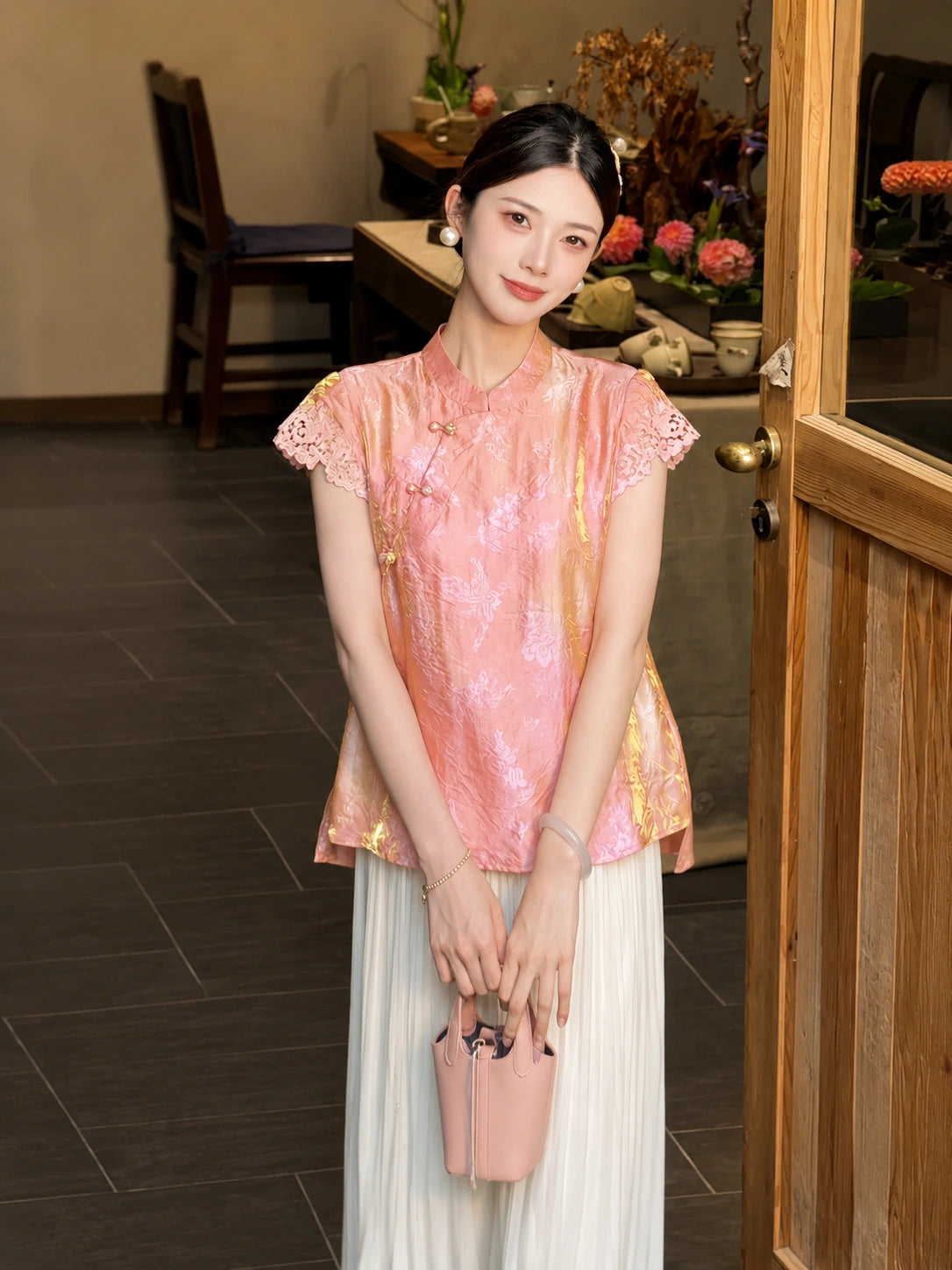 Model wearing a pink jacquard blouse with lace cap sleeves and a mandarin collar, holding a pink handbag, crafted from 80% Viscose and 20% Polyamide.