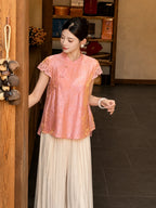Side profile of a pink short-sleeve Cheongsam blouse featuring gold floral jacquard pattern and lace trim, paired with flowy white pants.
