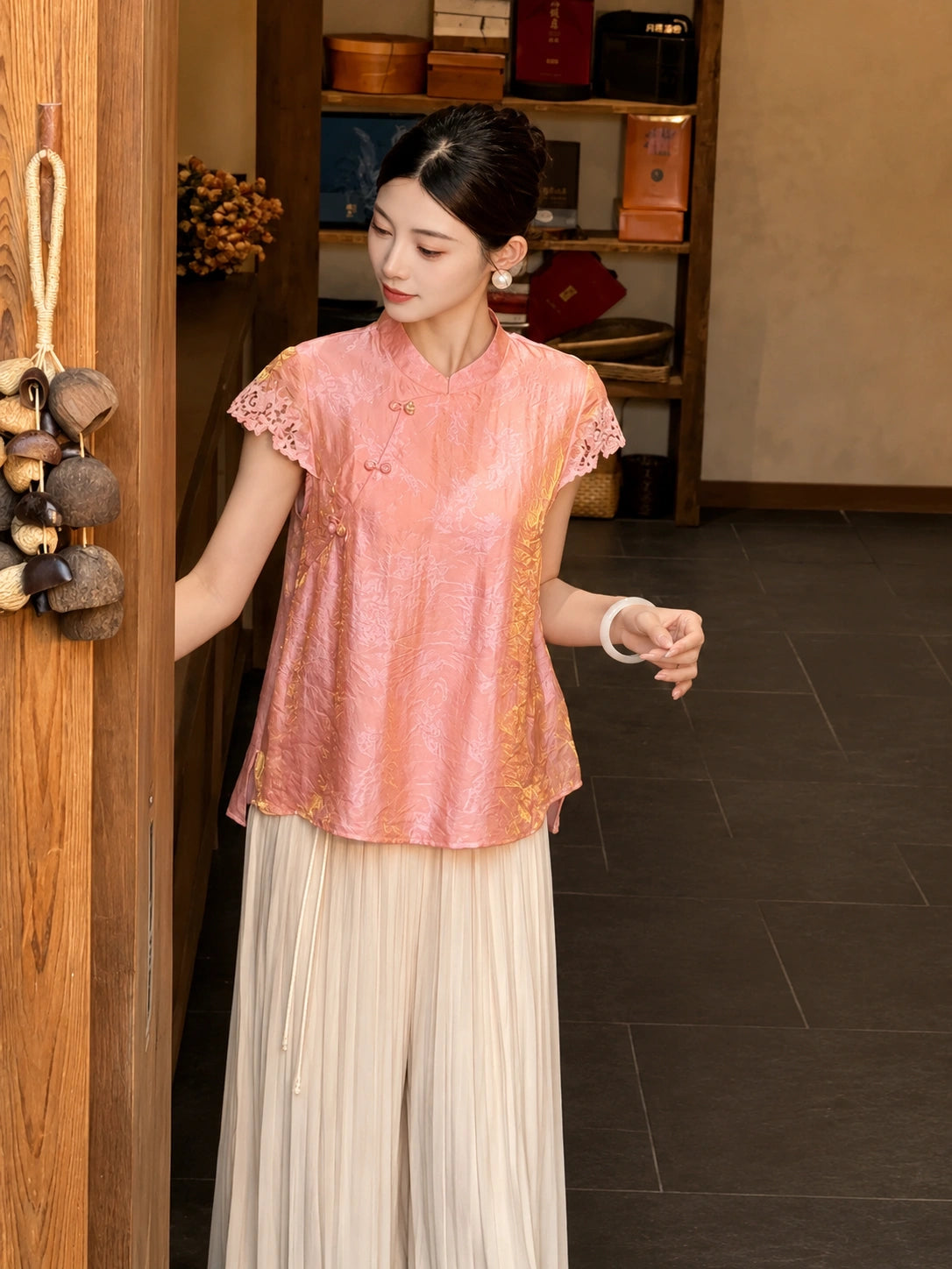 Side profile of a pink short-sleeve Cheongsam blouse featuring gold floral jacquard pattern and lace trim, paired with flowy white pants.