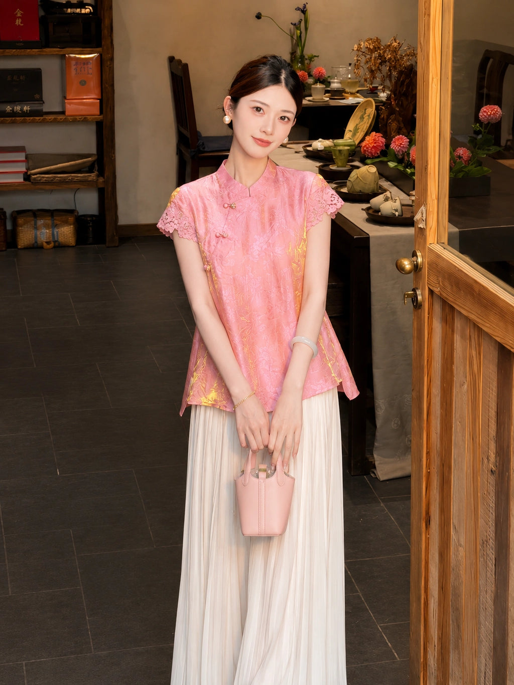 Front view of a pink Viscose-blend top with a mandarin collar, diagonal front closure, and lace cap sleeves, holding a pink handbag.