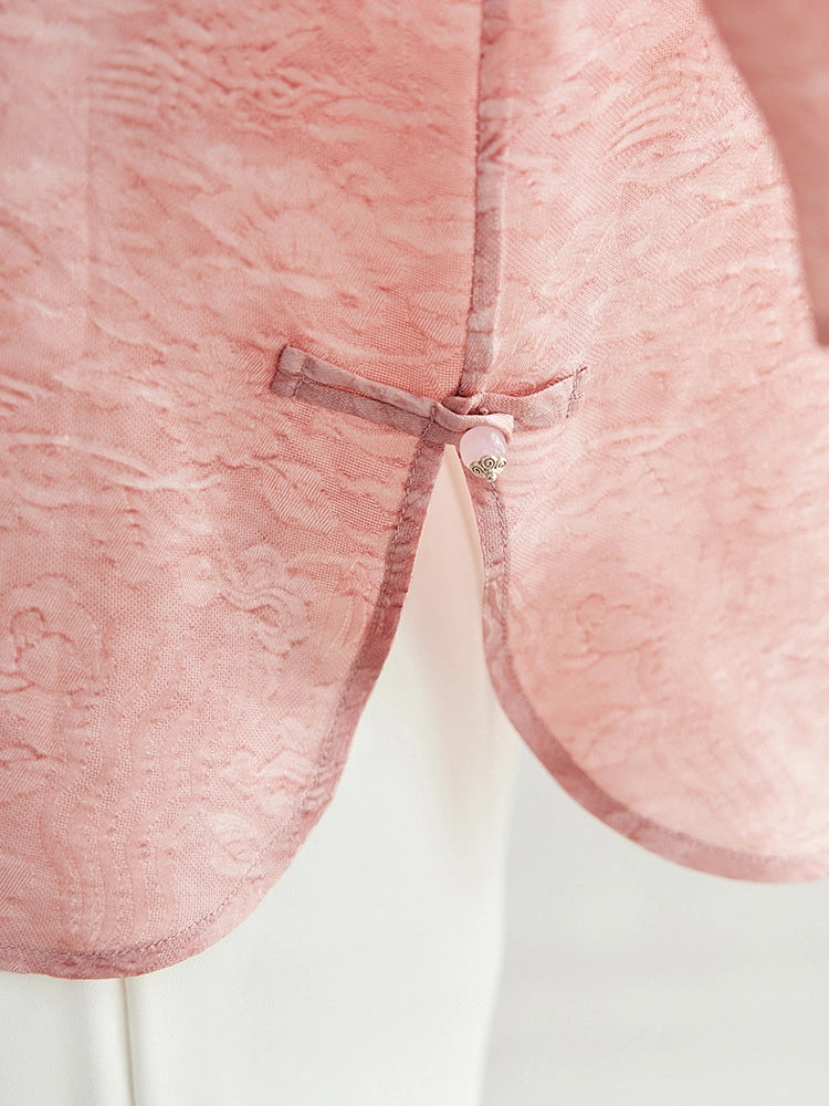 Close-up of a pink silk-blend top featuring a traditional frog button closure, showcasing the intricate texture and craftsmanship.