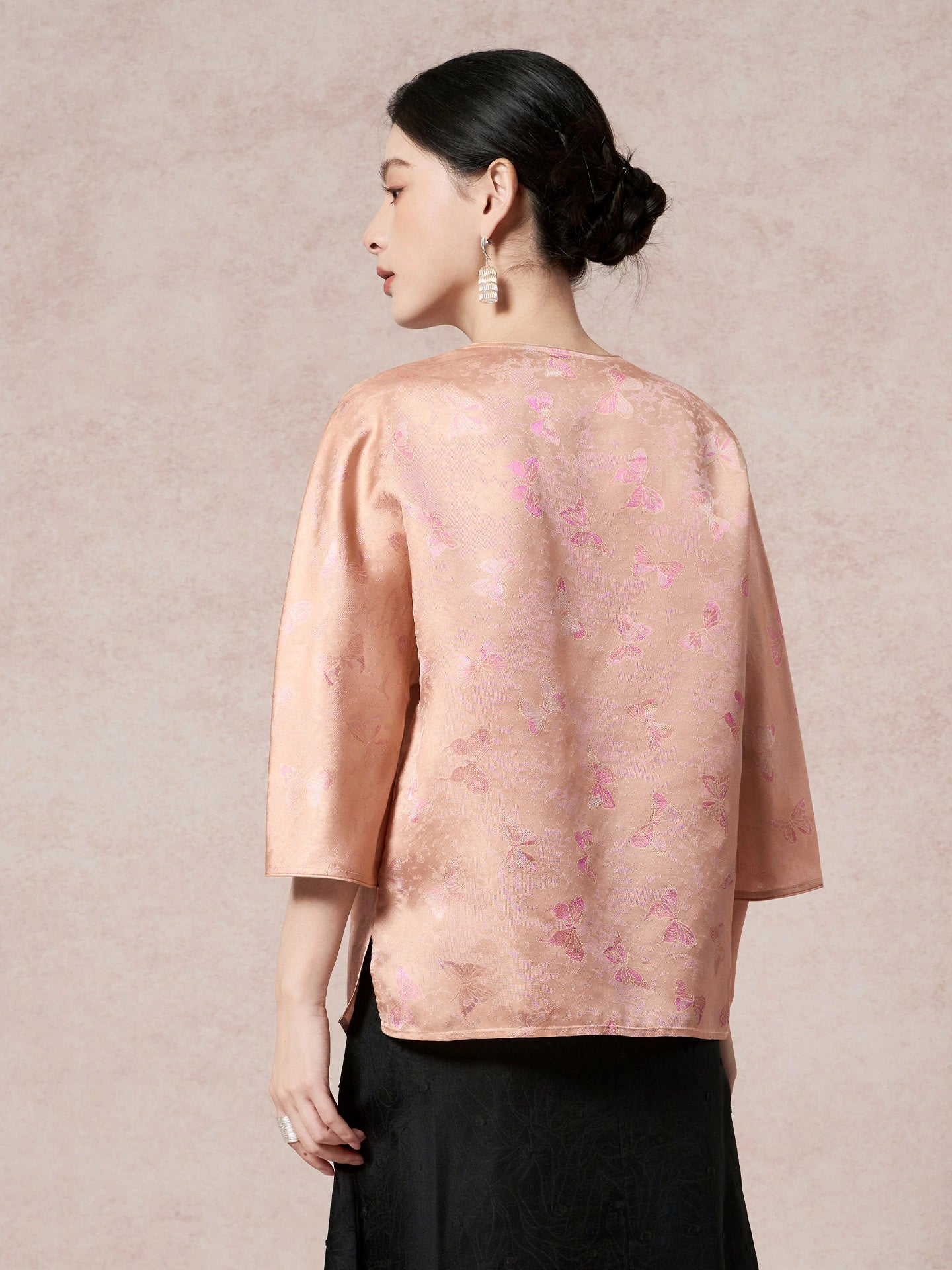 Back view of a pink-gold jacquard silk shirt featuring a butterfly pattern, a round neckline, and three-quarter sleeves, crafted from 100% mulberry silk.