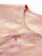 Close-up of the pink-gold silk fabric showing the intricate butterfly jacquard pattern and a delicate button detail on the diagonal placket.