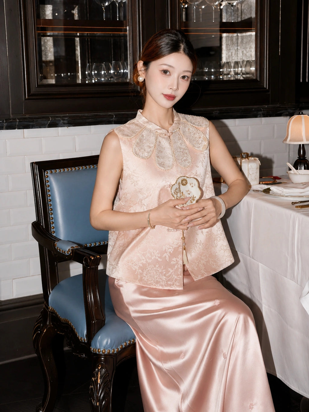 Model wearing a pink jacquard Cheongsam vest with pearl-trimmed scalloped collar, holding a fan, crafted from 70% Polyester and 30% Lyocell.