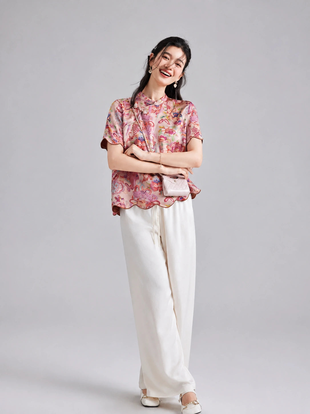 Woman wearing a pink koi and floral Xiangyunsha short-sleeve top with white wide-leg trousers