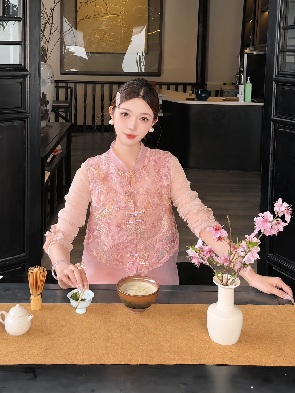 Close-up of a pink sleeveless vest with metallic embroidery, styled with a pink skirt and a white tea cup, highlighting the intricate details.