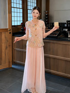 Model wearing pink pleated wide-leg pants with a layered lace hem, paired with an embroidered vest, holding a small object, showcasing the flowy silhouette.