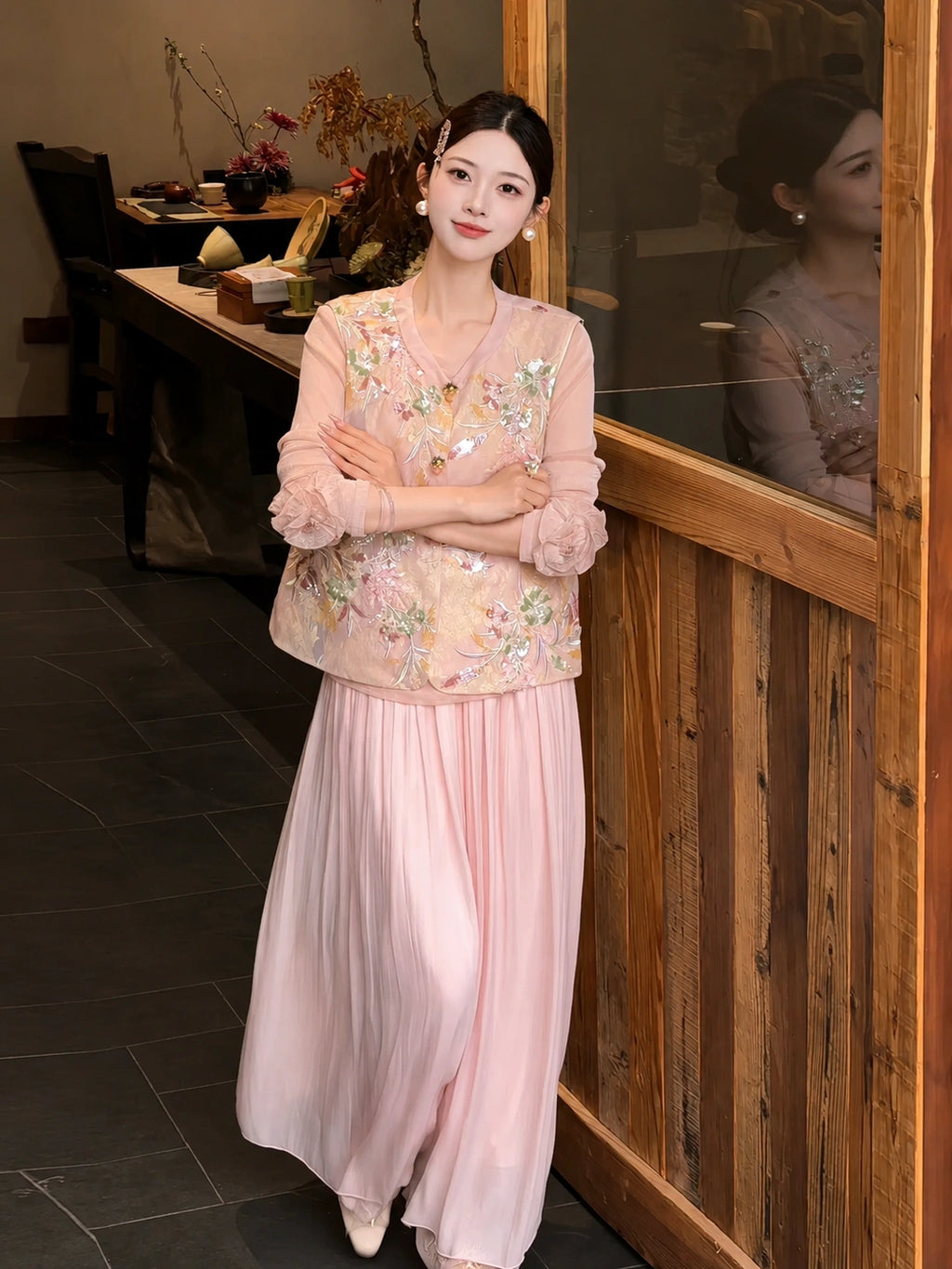 Front view of pink pleated wide-leg pants with a layered lace hem, styled with an embroidered vest and white shoes, highlighting the comfortable fit and elegant drape.