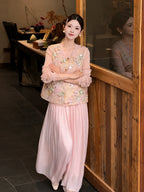 Front view of pink pleated wide-leg pants with a layered lace hem, styled with an embroidered vest and white shoes, highlighting the comfortable fit and elegant drape.