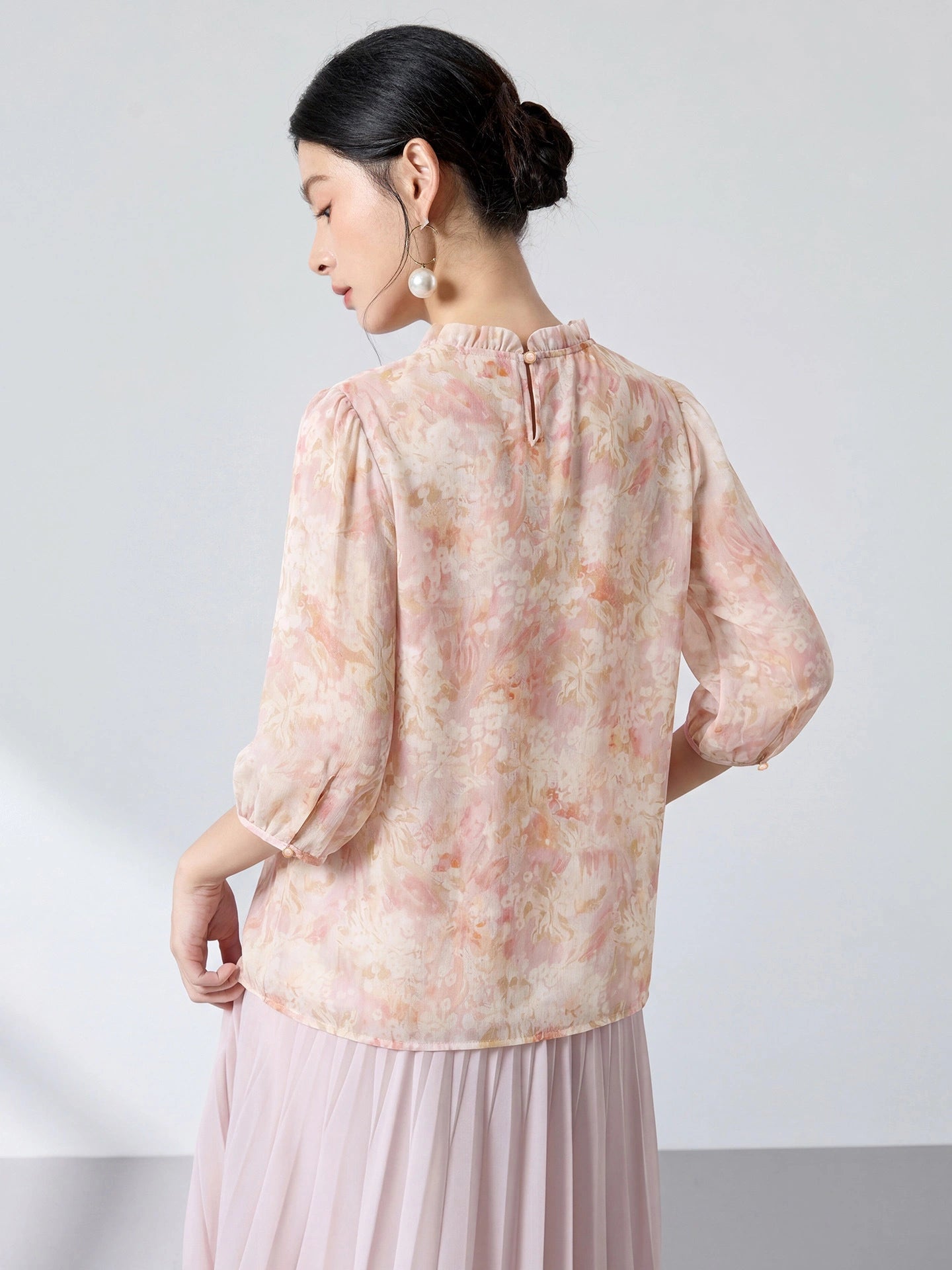 Back view of a pink floral print 100% mulberry silk blouse with a back button closure, paired with a light pink pleated skirt.